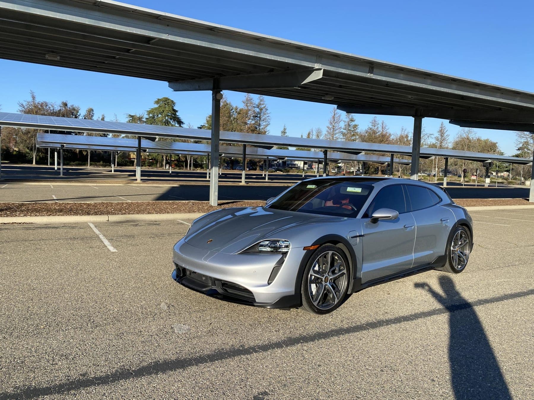 Silver Porsche Taycan Turbo Cross Turismo parked beneath a solar canopy, photographed from the front three-quarter