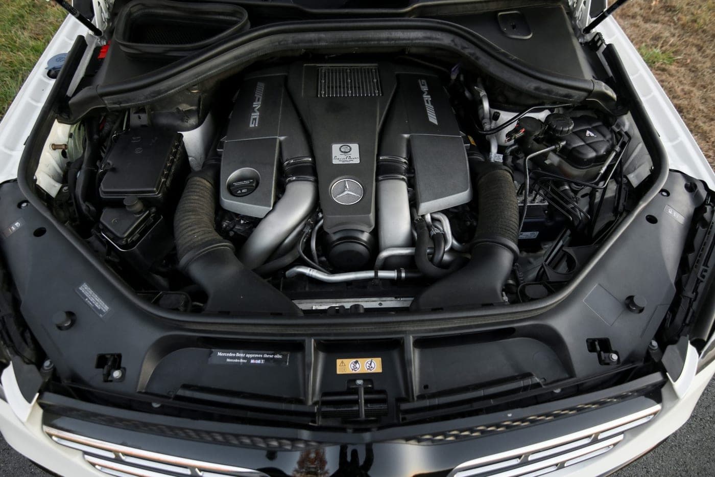 Open engine bay of a Mercedes-AMG GLS 63 showing the twin-turbo V8 and AMG engine cover