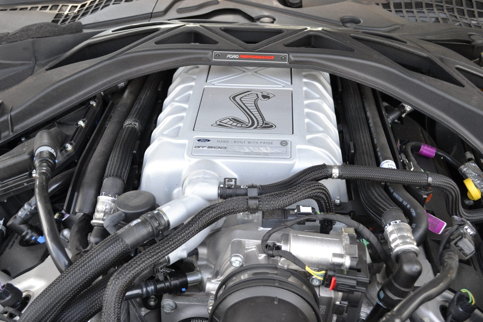 Open engine bay of a Ford Mustang Shelby GT500 showing the supercharger housing and Shelby-badged intake