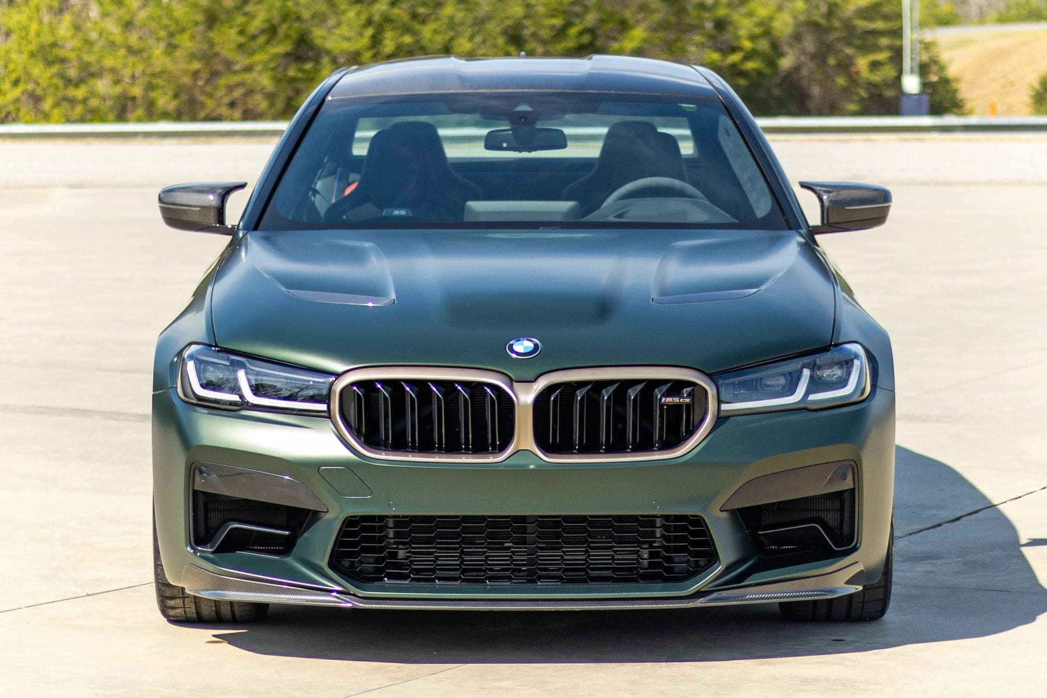 Matte green BMW M5 CS photographed head-on, showing the grille and gold-finished wheels — from a Carviondealer listing