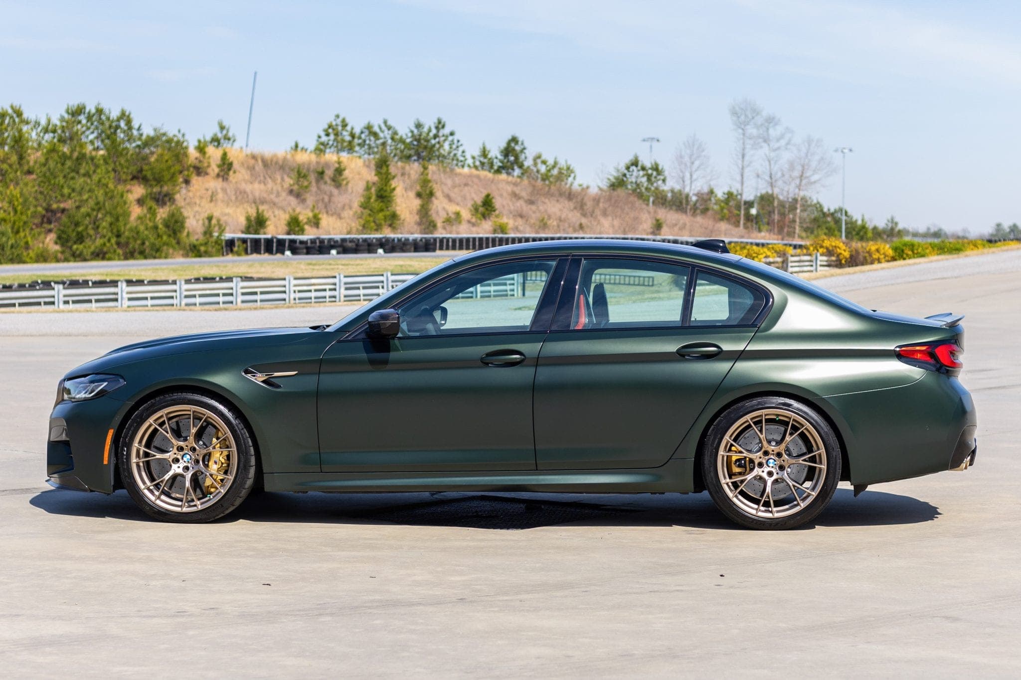 Matte green BMW M5 CS in side profile on tarmac under overcast light