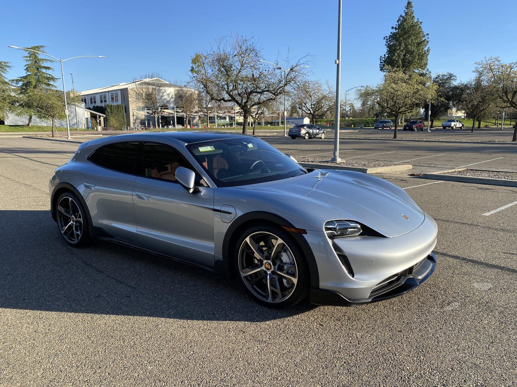 Silver Porsche Taycan Turbo Cross Turismo photographed from the front three-quarter in an open car park