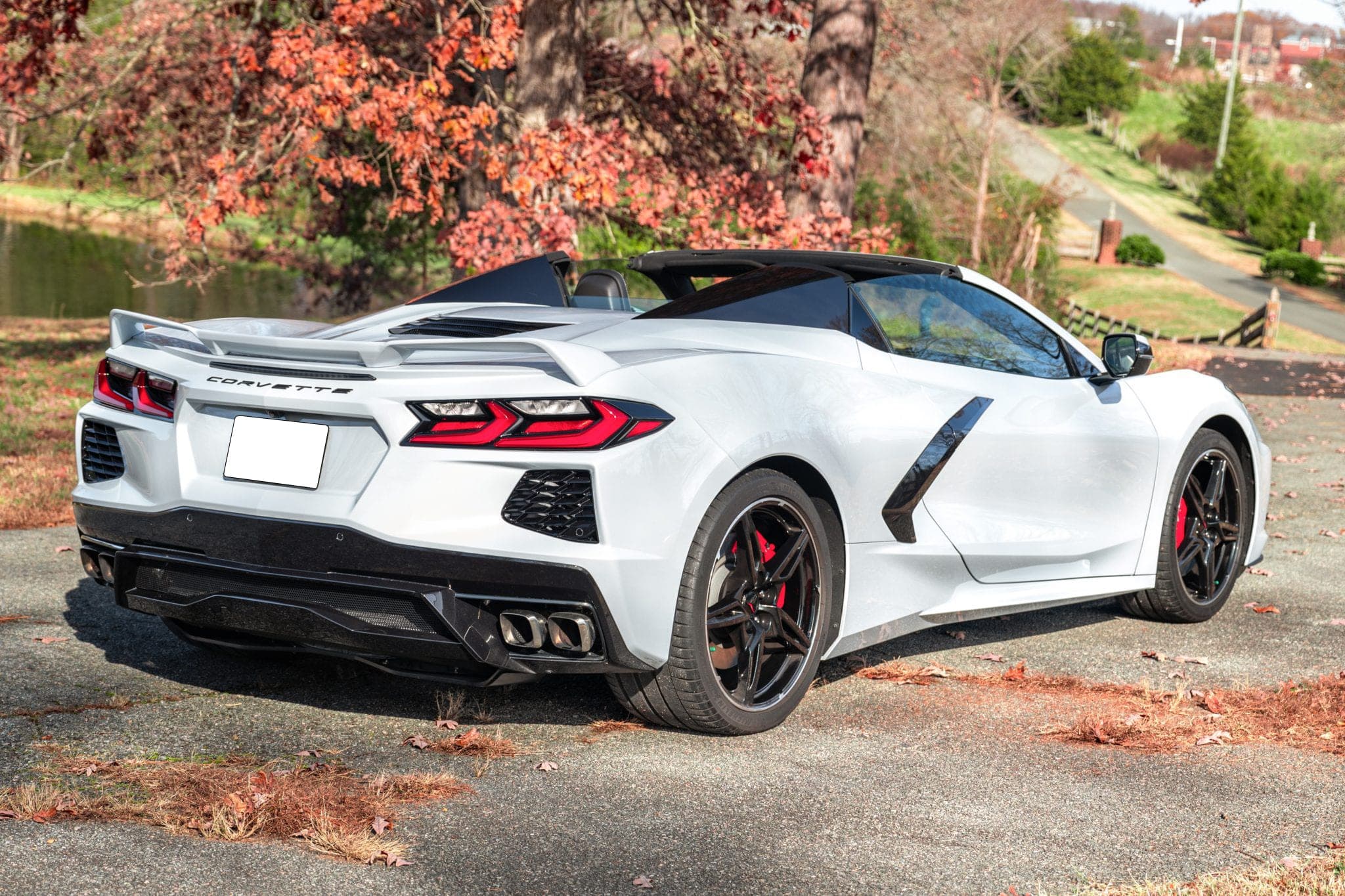 White Corvette Stingray convertible photographed from directly behind on a leaf-strewn drive, quad exhausts and rear diffuser in frame