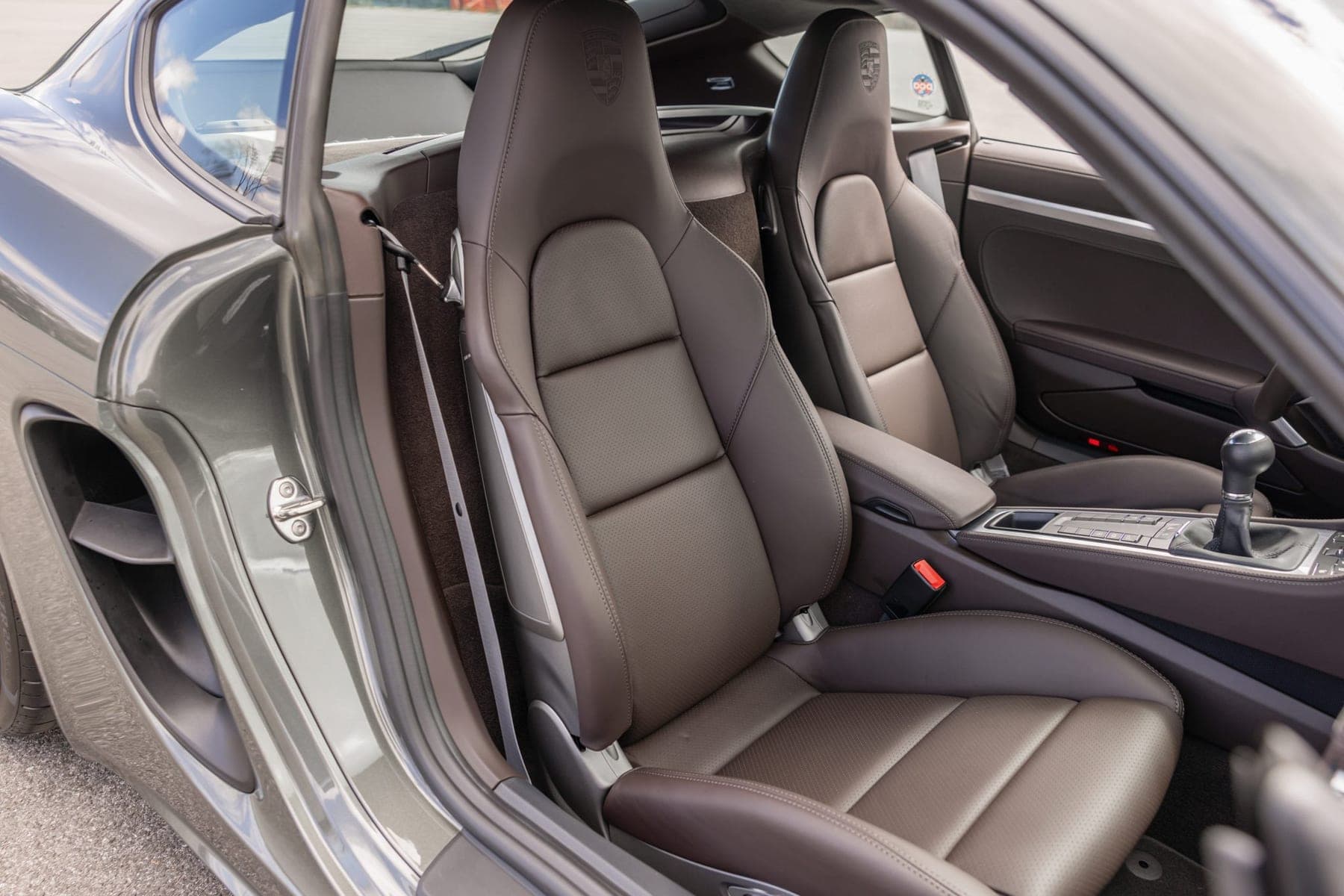 Espresso brown leather cabin of a Porsche 718 Cayman GTS 4.0, both seats and the manual gear lever visible through the open door