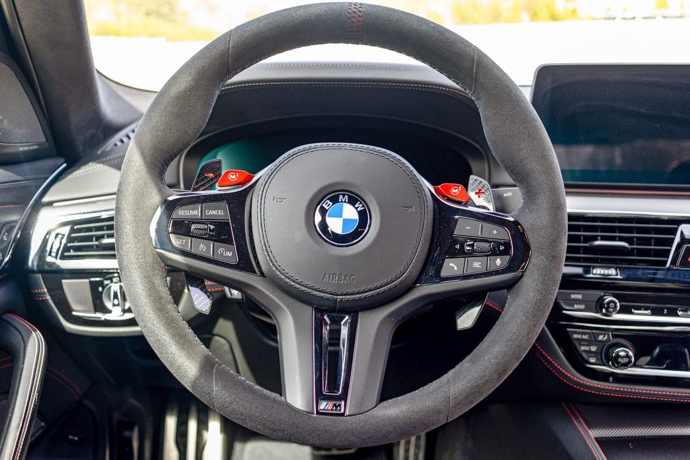Alcantara steering wheel with red M1 and M2 drive-mode buttons in a BMW M5 CS
